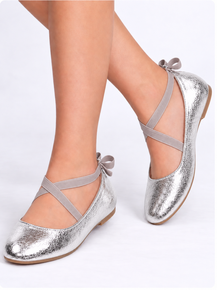 Girl wearing silver metallic ballet flats with crisscross straps and bow details