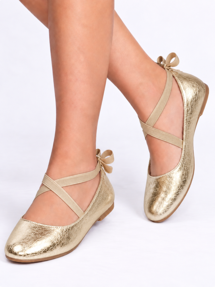 Girl wearing gold metallic ballet flats with crisscross straps and bow details