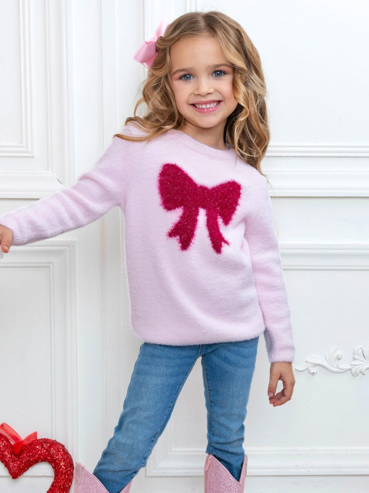 Little girl wearing a pink sweater with fuzzy bow design styled with jeans