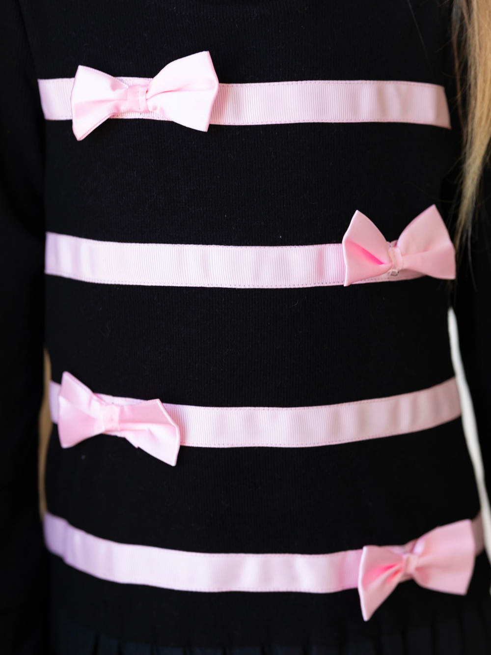 Girls black pleated sweater dress featuring pink ribbon and bow details.