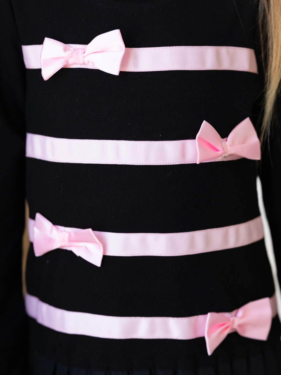 Girls black pleated sweater dress featuring pink ribbon and bow details.