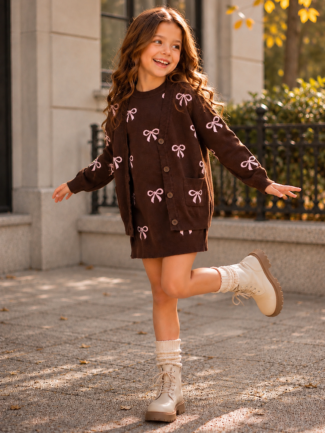 Girl wearing a chocolate brown knit dress and matching cardigan with pink bows.