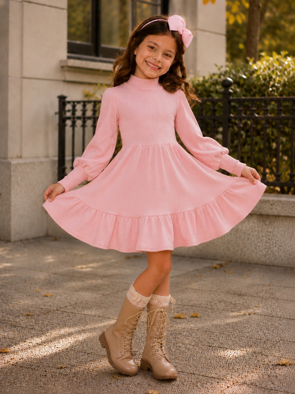 Girl wearing a blush ribbed long sleeve twirl dress with ruffle hem and boots.