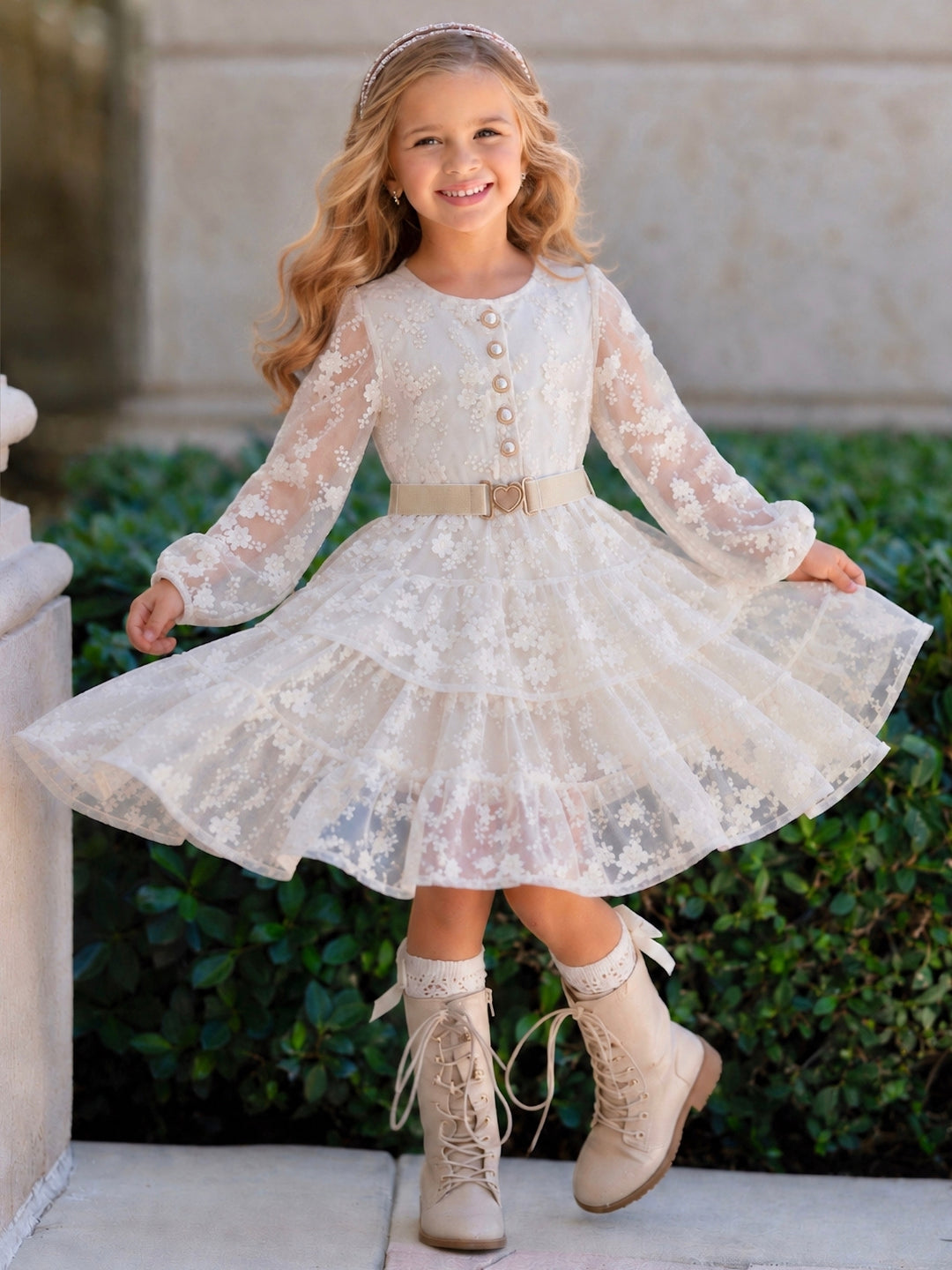 Girl wearing an ivory tiered dress with matching belt and puff sleeves.