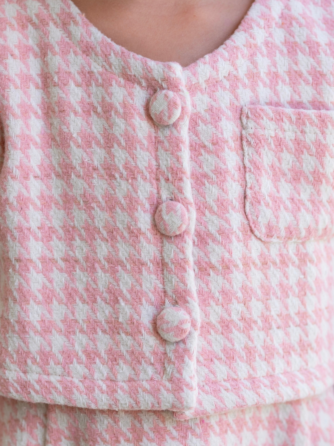 Close-up of a pink and ivory houndstooth jacket featuring decorative covered buttons and a front pocket.