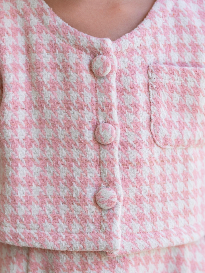 Close-up of a pink and ivory houndstooth jacket featuring decorative covered buttons and a front pocket.