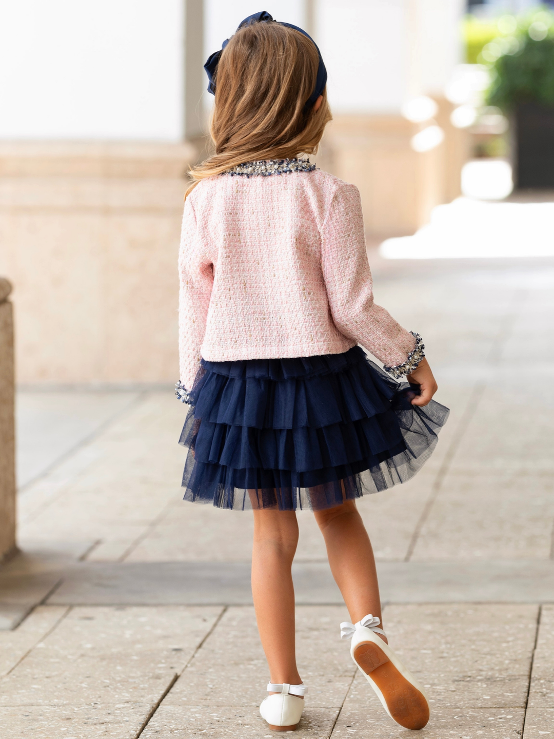 Girl wearing a blush tweed jacket and a navy layered tulle skirt for special occasions.