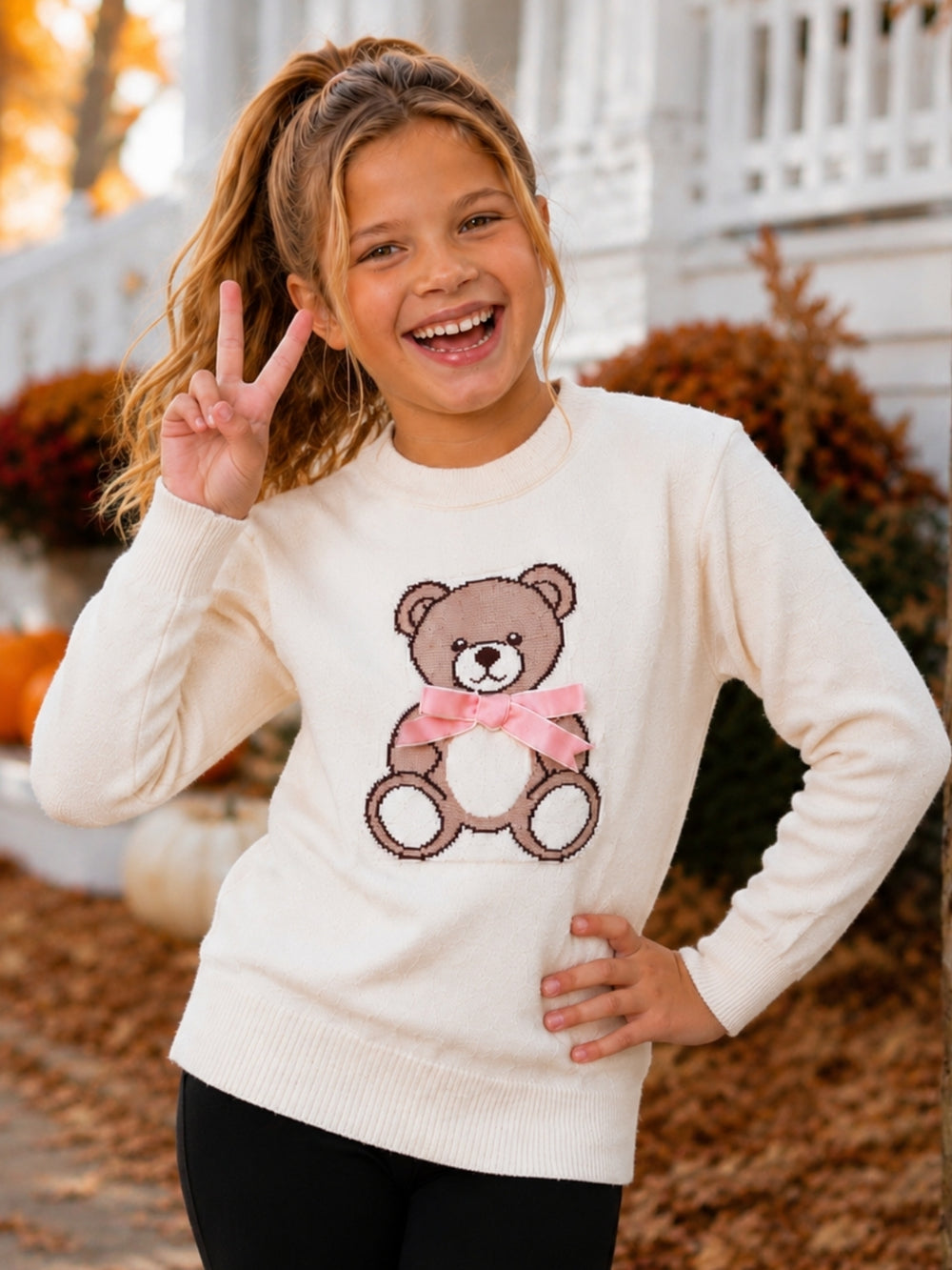 Girl wearing an ivory teddy bear knit sweater with a pink bow.