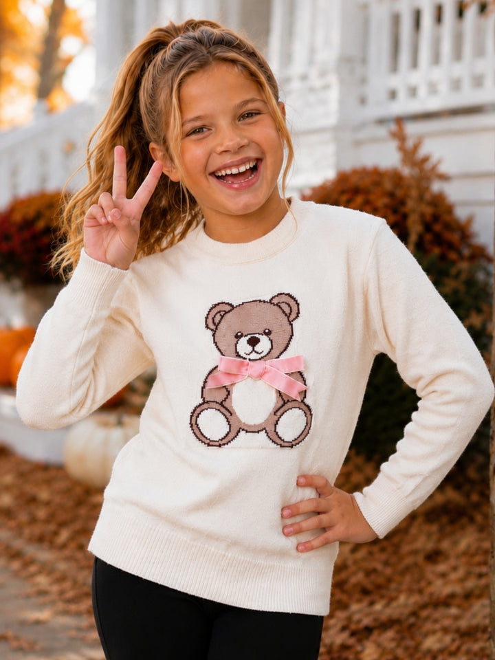 Girl wearing an ivory teddy bear knit sweater with a pink bow.